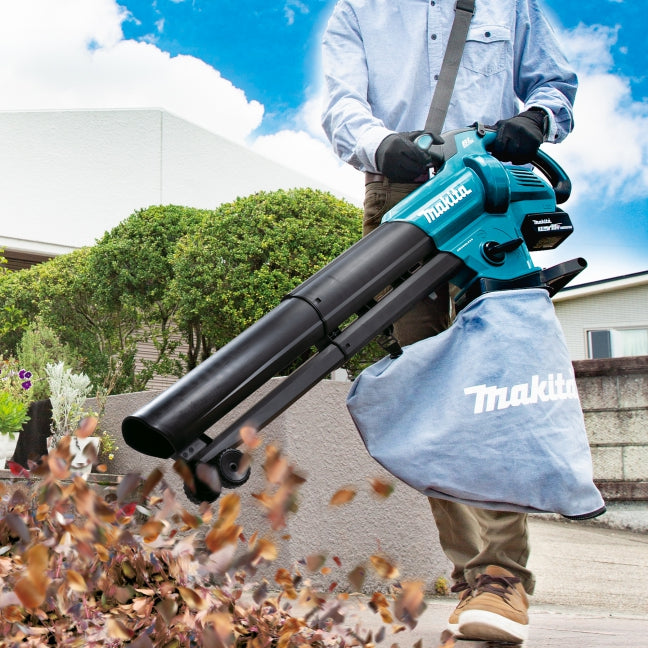 Person using a Makita leaf blower to clear leaves outdoors.