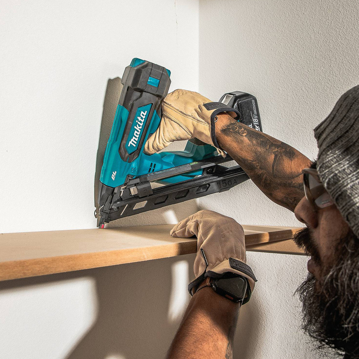Person using a Makita nail gun on a wooden shelf against a white wall.