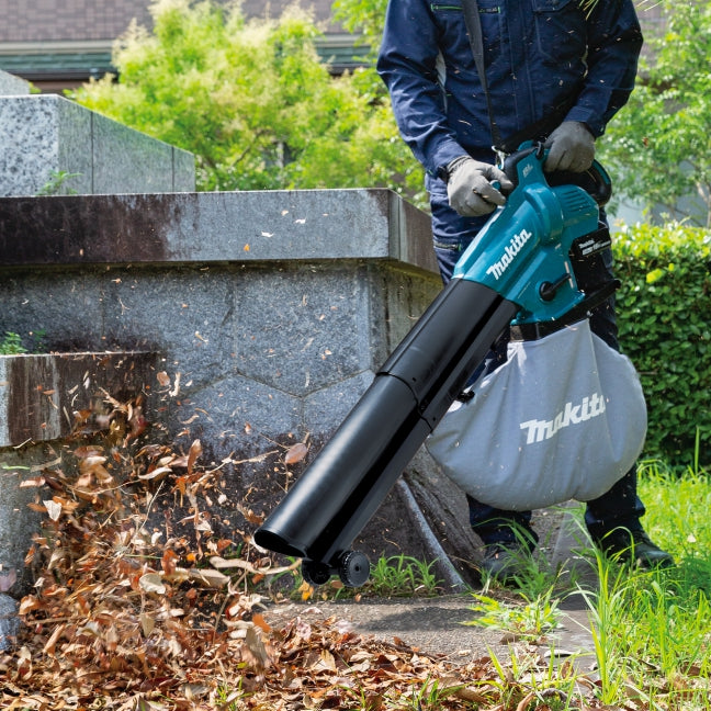 Person using a Makita leaf blower to clear leaves from a garden area.
